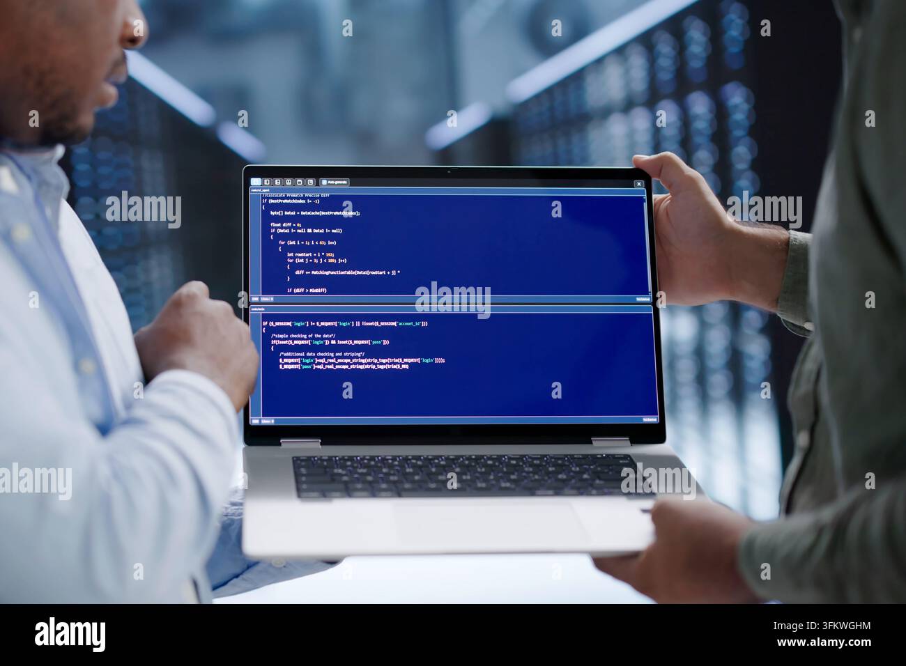 Programmer Reviews Code Security Details While Working In Busy Server Room. Stock Photo