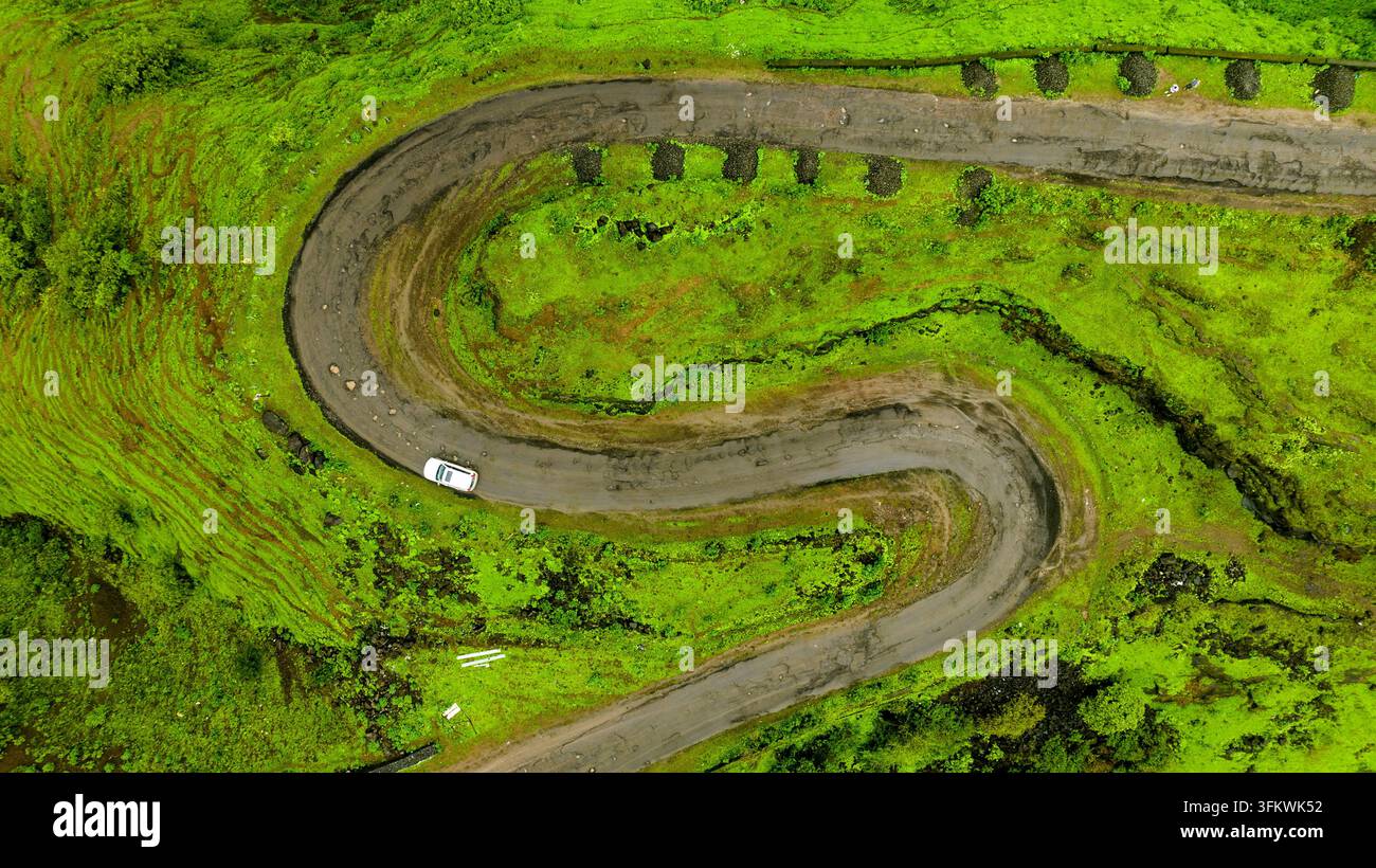 Aerial view of a winding S-shaped road cutting through lush green hills ...