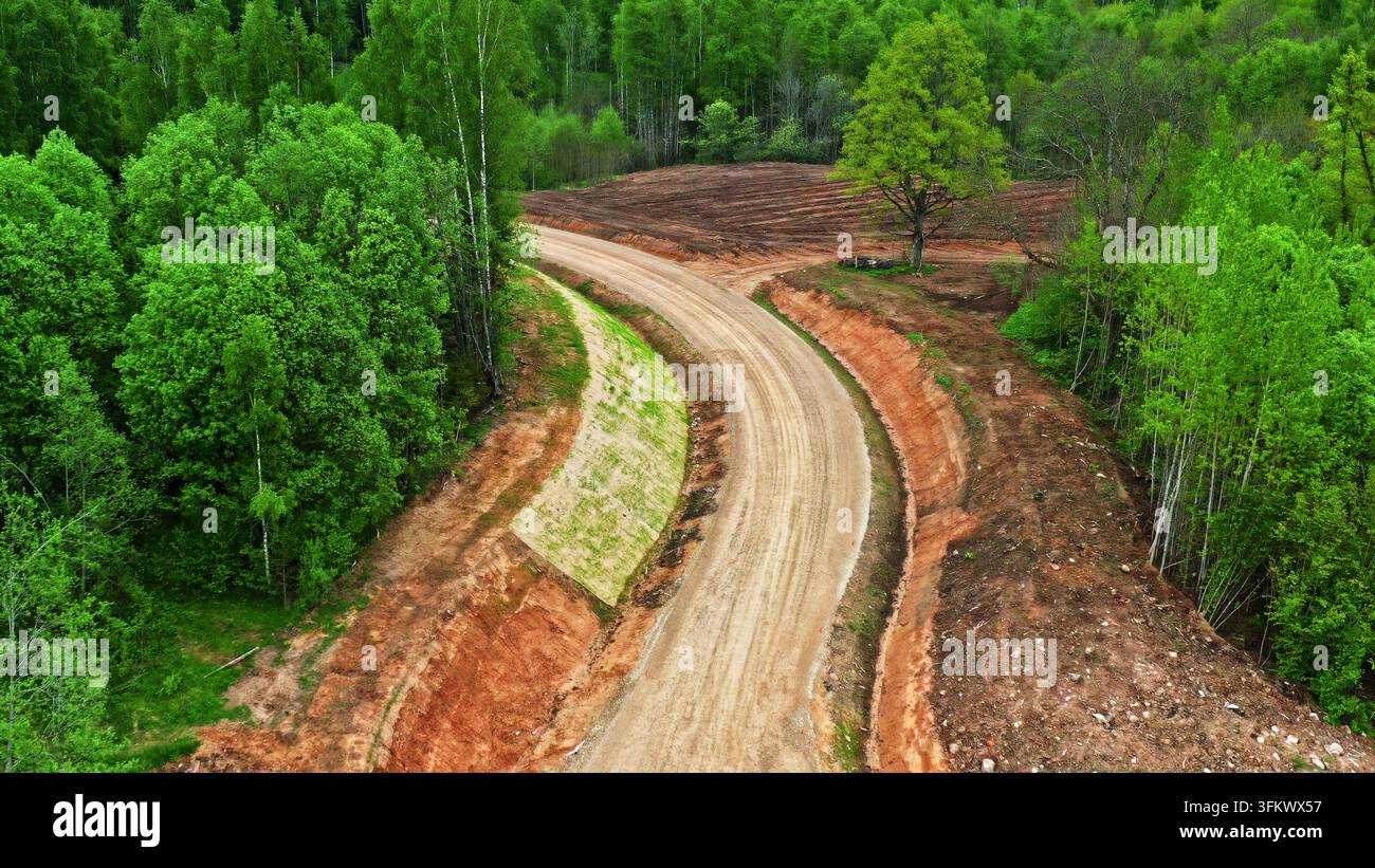 Aerial view of a winding dirt road cutting through a dense green forest ...