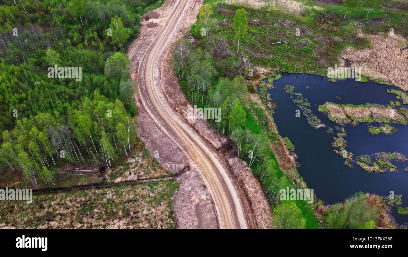 Aerial view of a dirt access road winding through a lush green forest ...