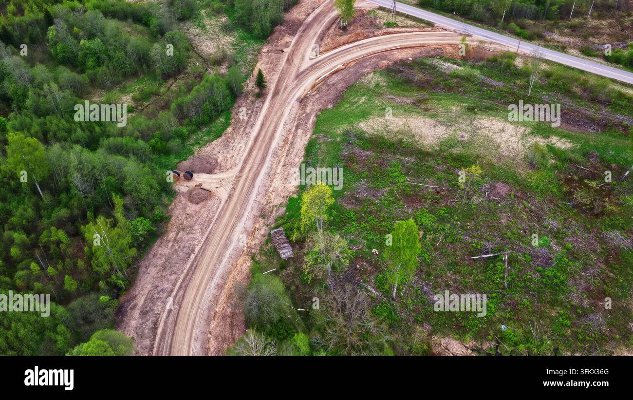 Aerial view of a dirt access road winding through a lush green forest ...