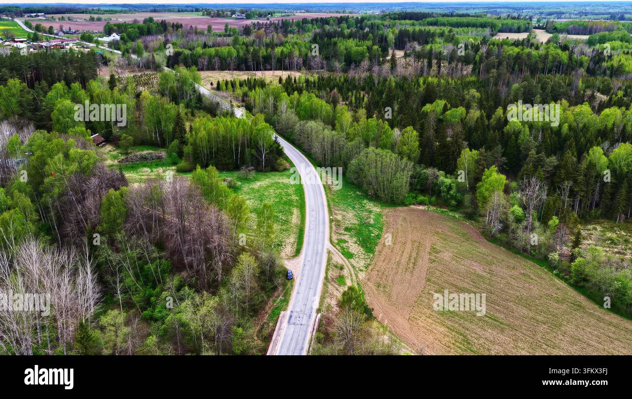 Aerial view of a winding road cutting through a dense green forest and ...