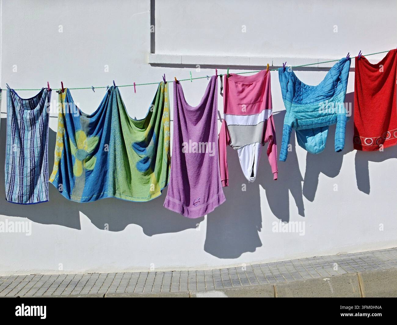 Colorful laundry hanging on a clothesline against a white wall with shadows Stock Photo