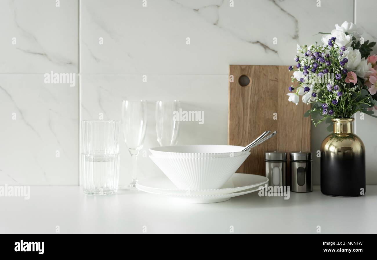Minimal white table setting with bowls, glasses and flowers on kitchen counter in bright modern interior Stock Photo