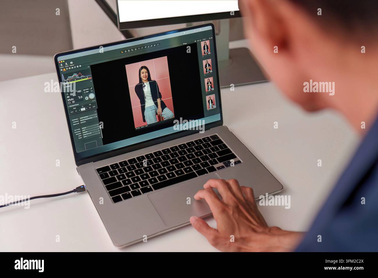 Over the shoulder view of creative photographer using image editing software on laptop to retouch female portrait photo Stock Photo
