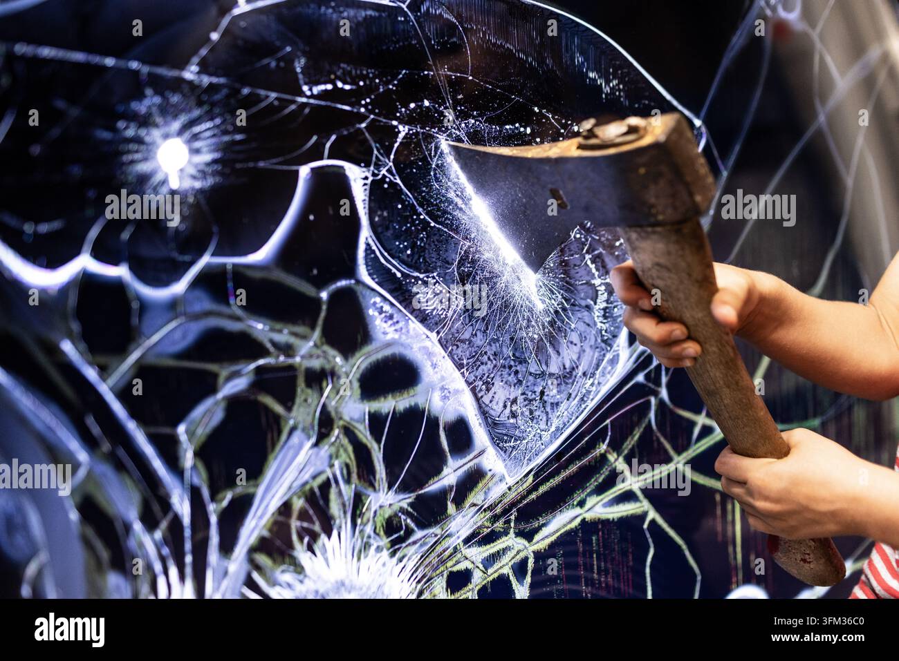 Someone strikes a shattered glass panel using a wooden axe Stock Photo