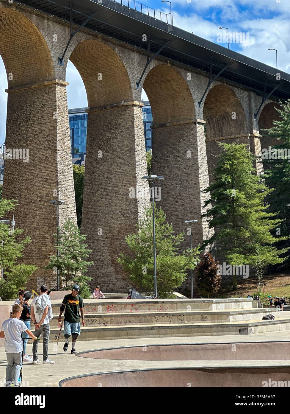 Massive stone viaduct bridge overlooking an urban skatepark with people. Low angle view of a huge historic stone arch viaduct with towering pillars to - Smartphone Captured Stock Image
