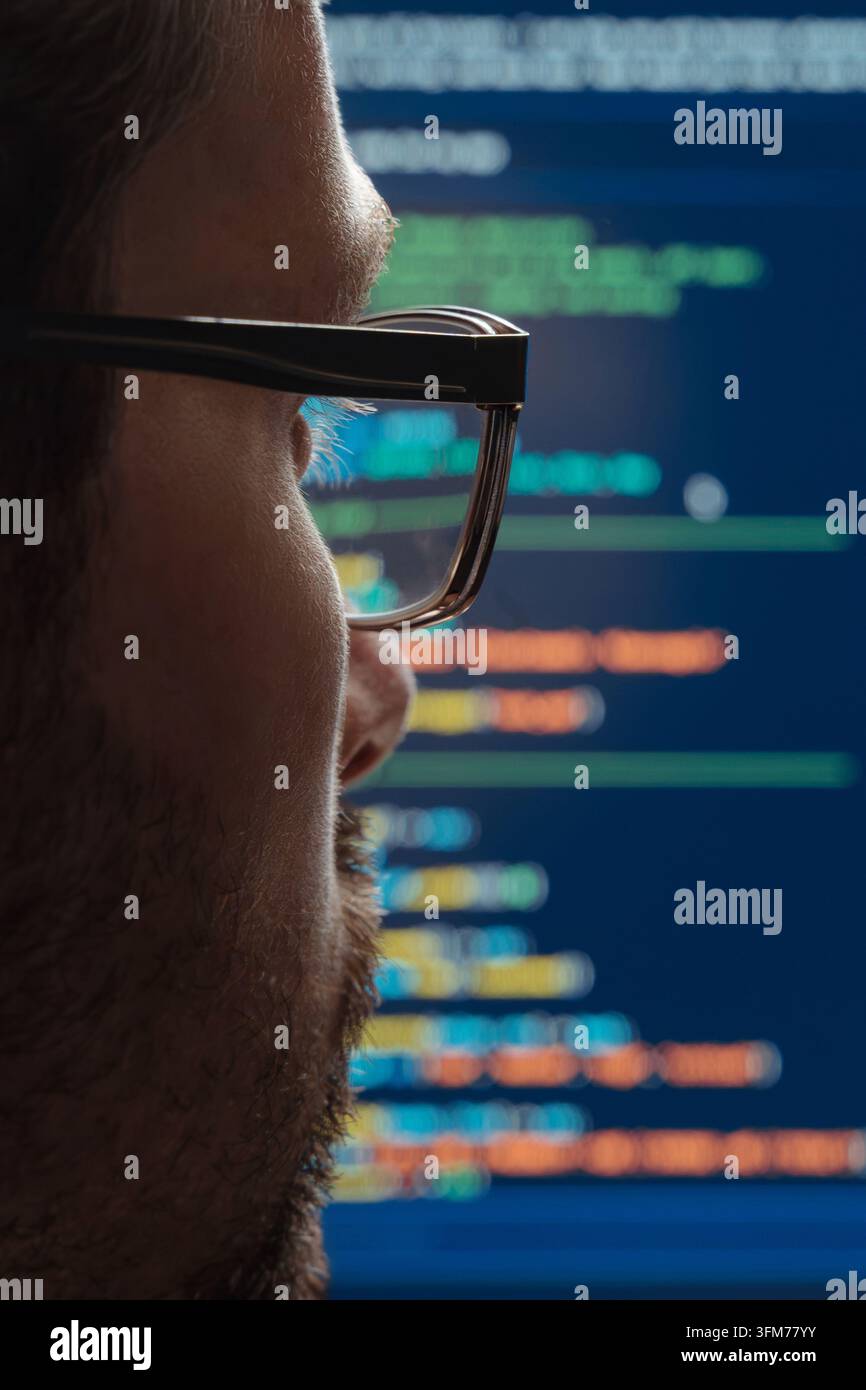 Rear view close up of a programmer in eyeglasses looking at screen with running programming code lines, working on machine learning or artificial intelligence development. Stock Photo