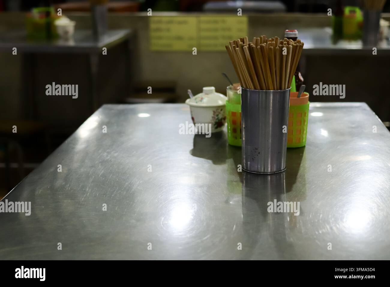 Empty stainless steel dining table with stainless chopstick holder, condiment set and covered ceramic container at a Thai restaurant. Stock Photo