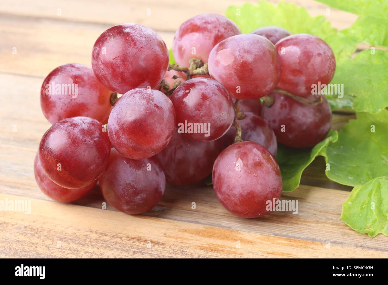 Fresh Red Globe Grapes Bunch with Leaves on Wooden Table Surface Stock Photo