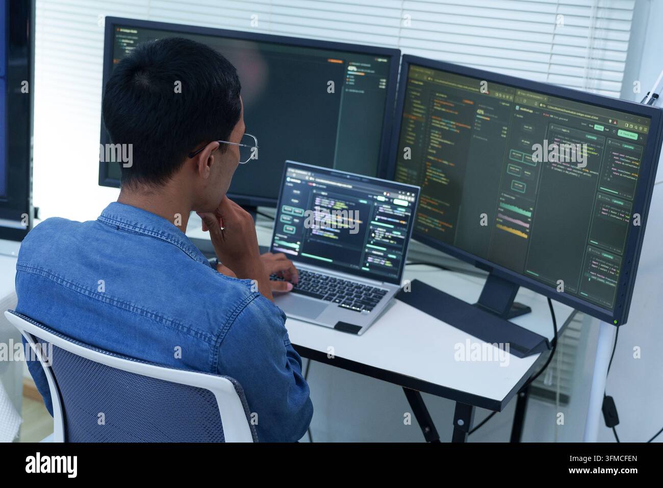 Programmer Developing Software with Code on Multiple Screens Stock Photo