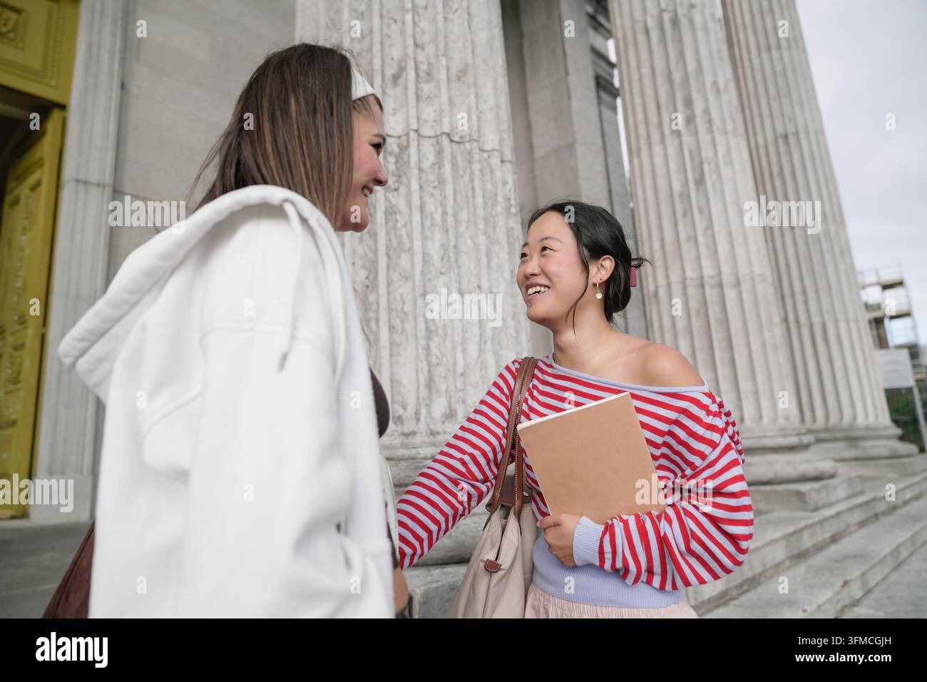 Diverse students talking and laughing on university campus Stock Photo