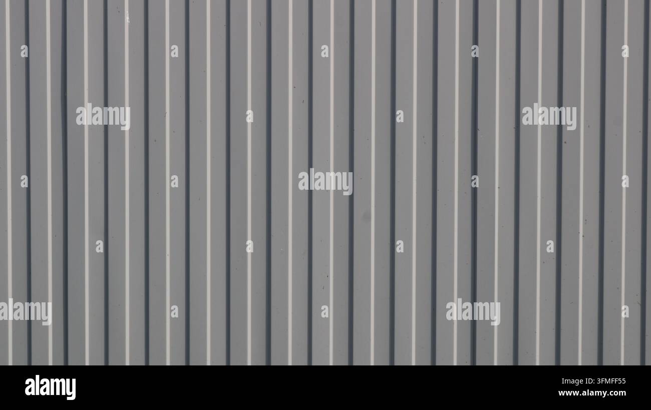 A background of vertical gray corrugated metal sheeting. The surface features a distinct geometric relief with alternating raised ribs and shadows Stock Photo