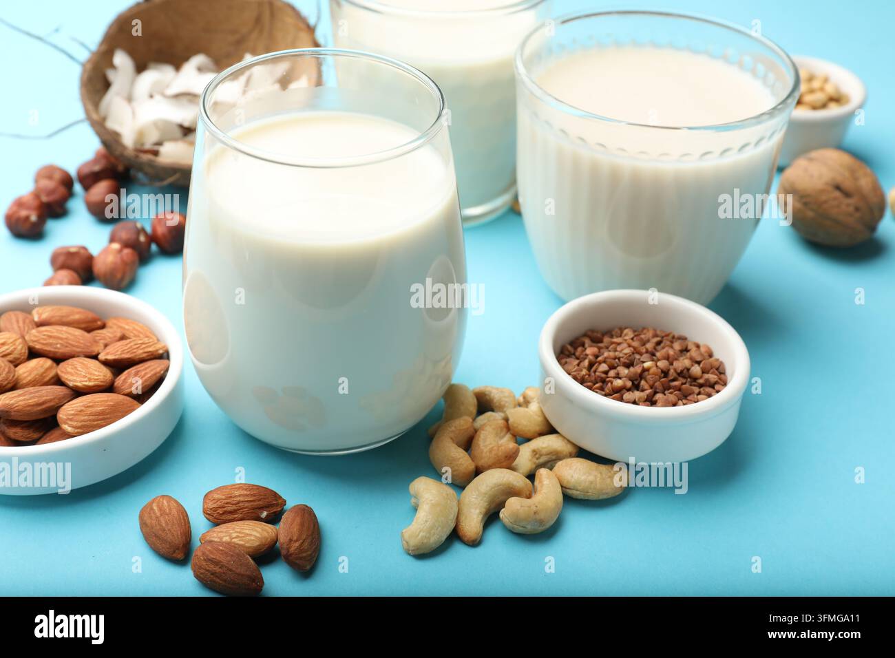 Different types of vegan milk in glasses and ingredients on light blue ...