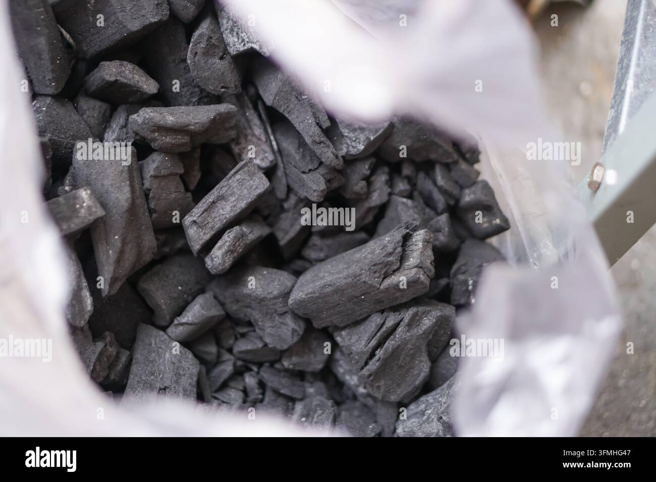 Close-up view of black charcoal pieces inside an open white bag ...