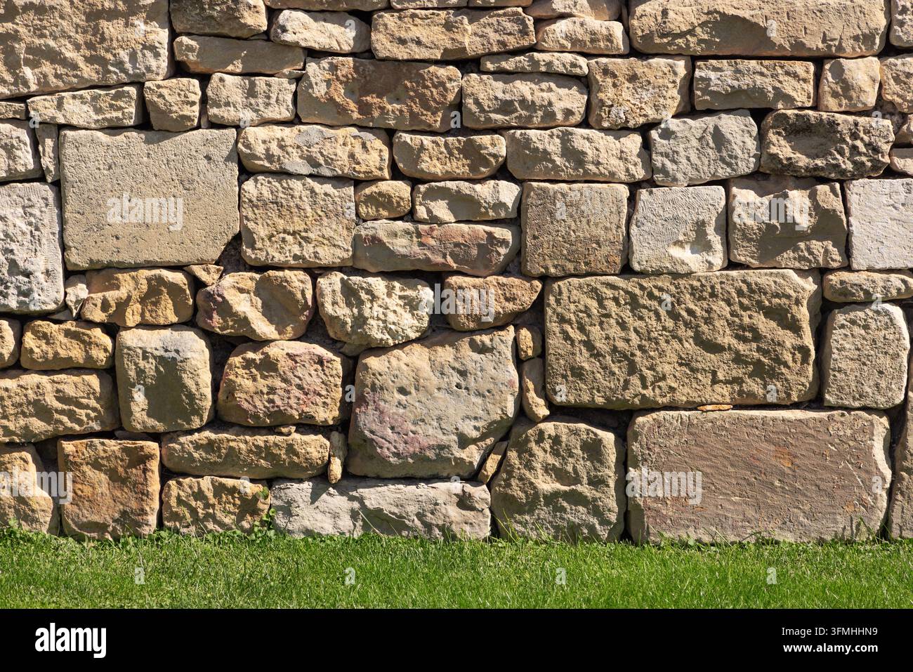 Rough old stone wall texture with green grass foreground Stock Photo