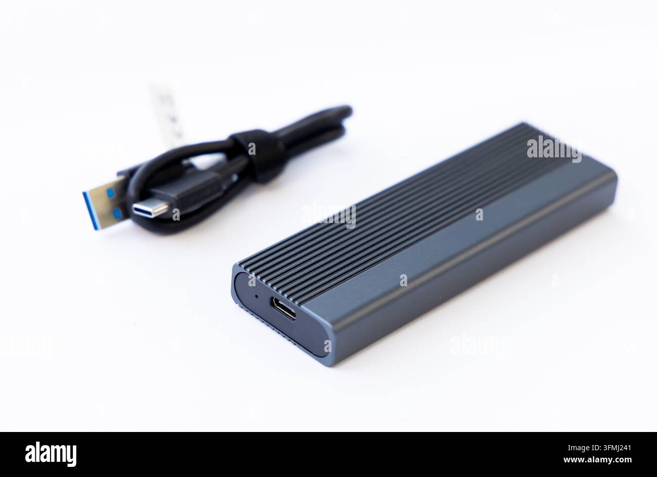 An external solid state drive sits next to its connecting cord Stock Photo