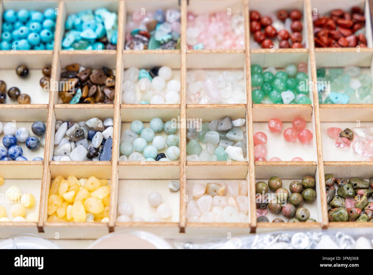 A wooden box holds many colorful gemstone beads Stock Photo