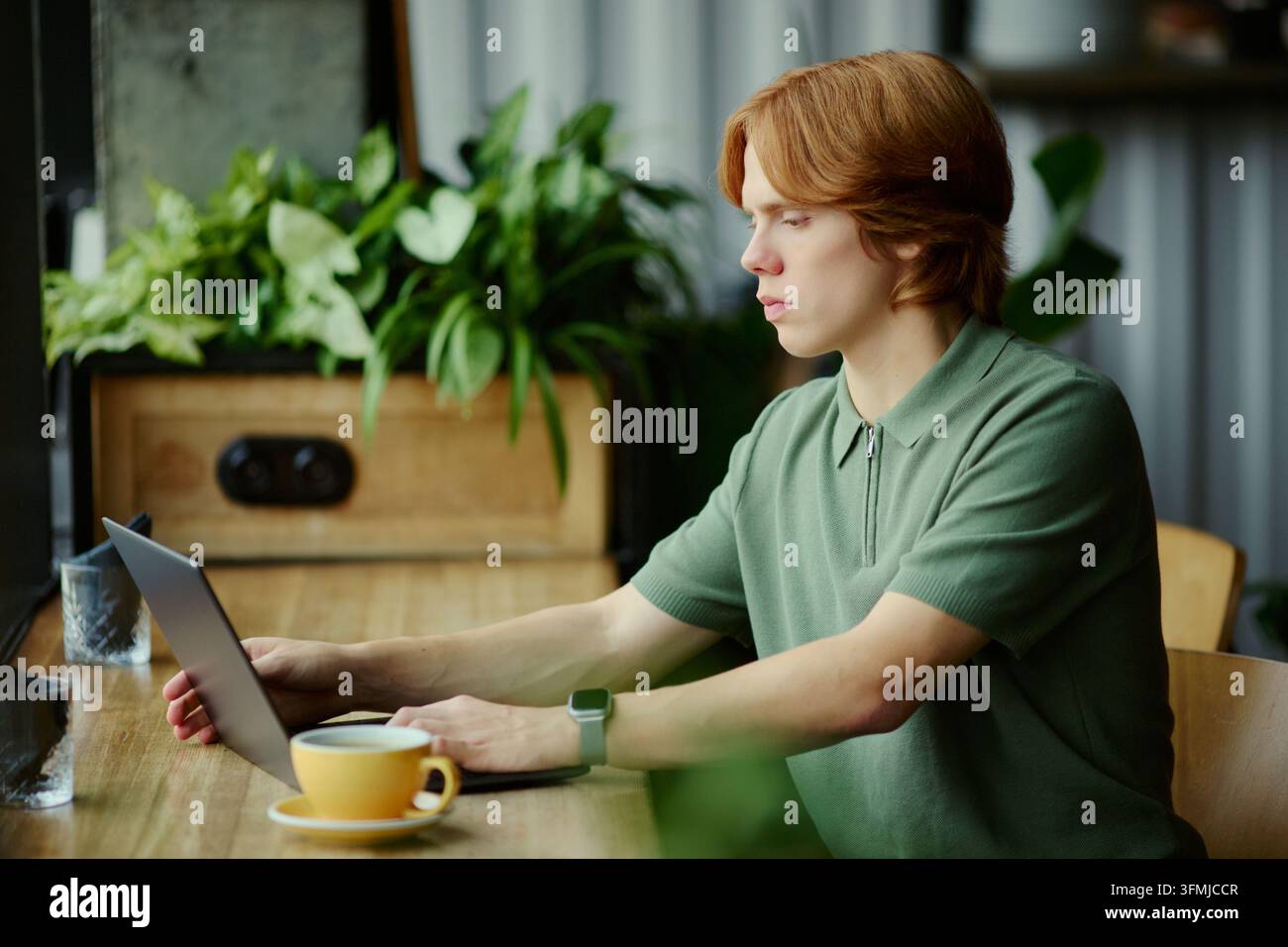 Man Working on Laptop Computer While Sitting at Modern Cafe Table Stock Photo
