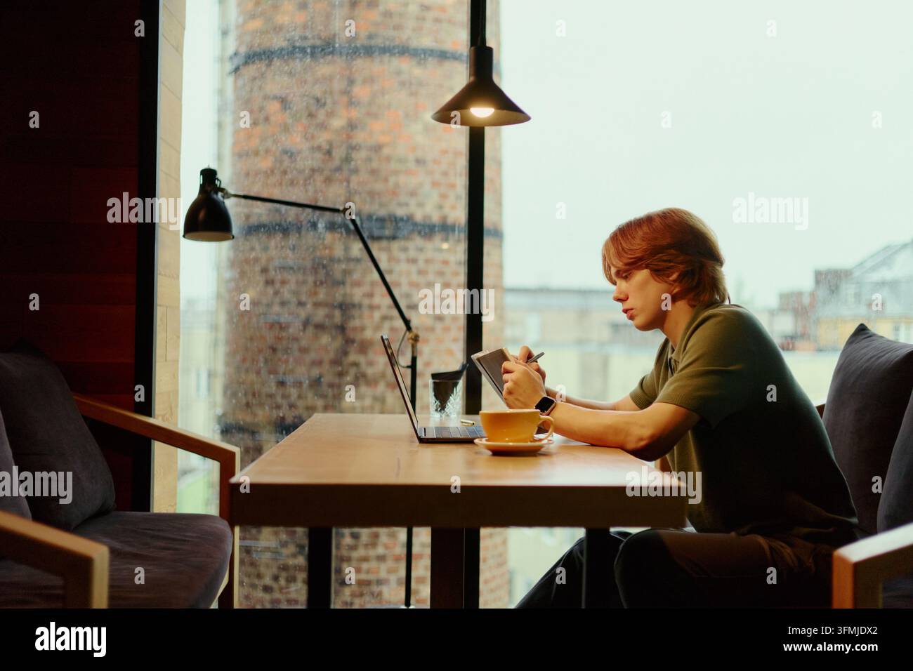 Man Writing in Notebook While Working on Laptop in Cafe Stock Photo