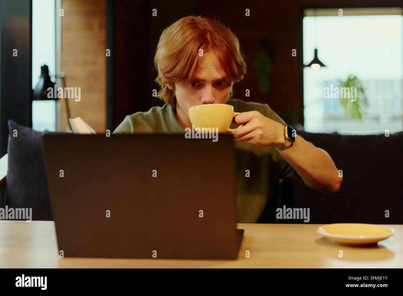 Man Drinking Coffee While Working on Laptop in Cafe Stock Photo