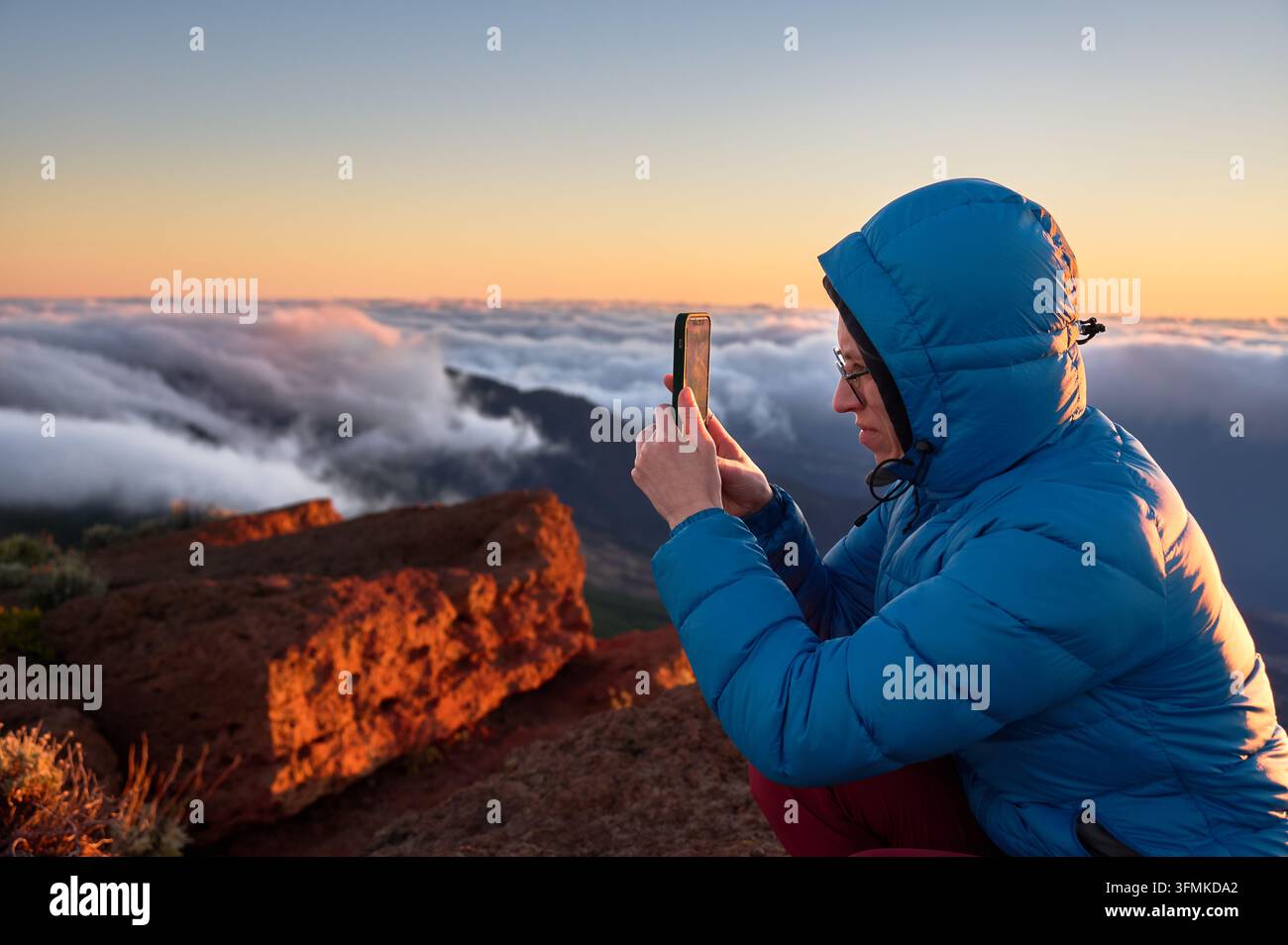 Woman uses smartphone to photograph dramatic sea of clouds from high ...