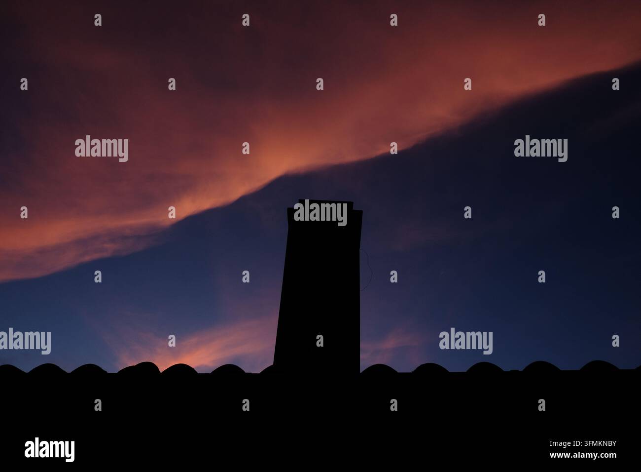 A dramatic sunset illuminates the sky with scattered clouds over ...
