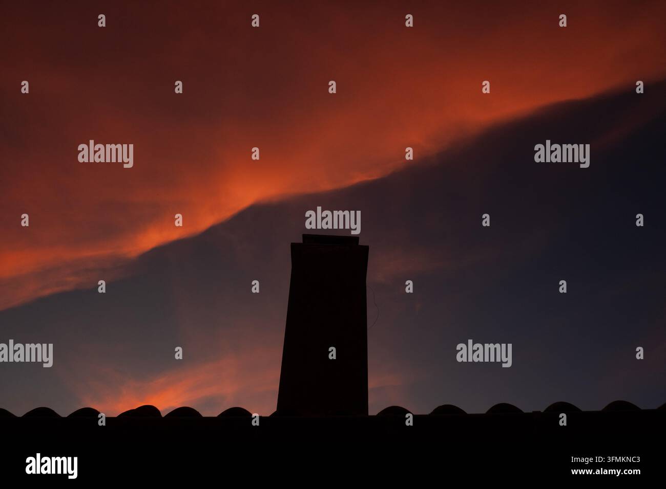 A dramatic sunset illuminates the sky with scattered clouds over ...