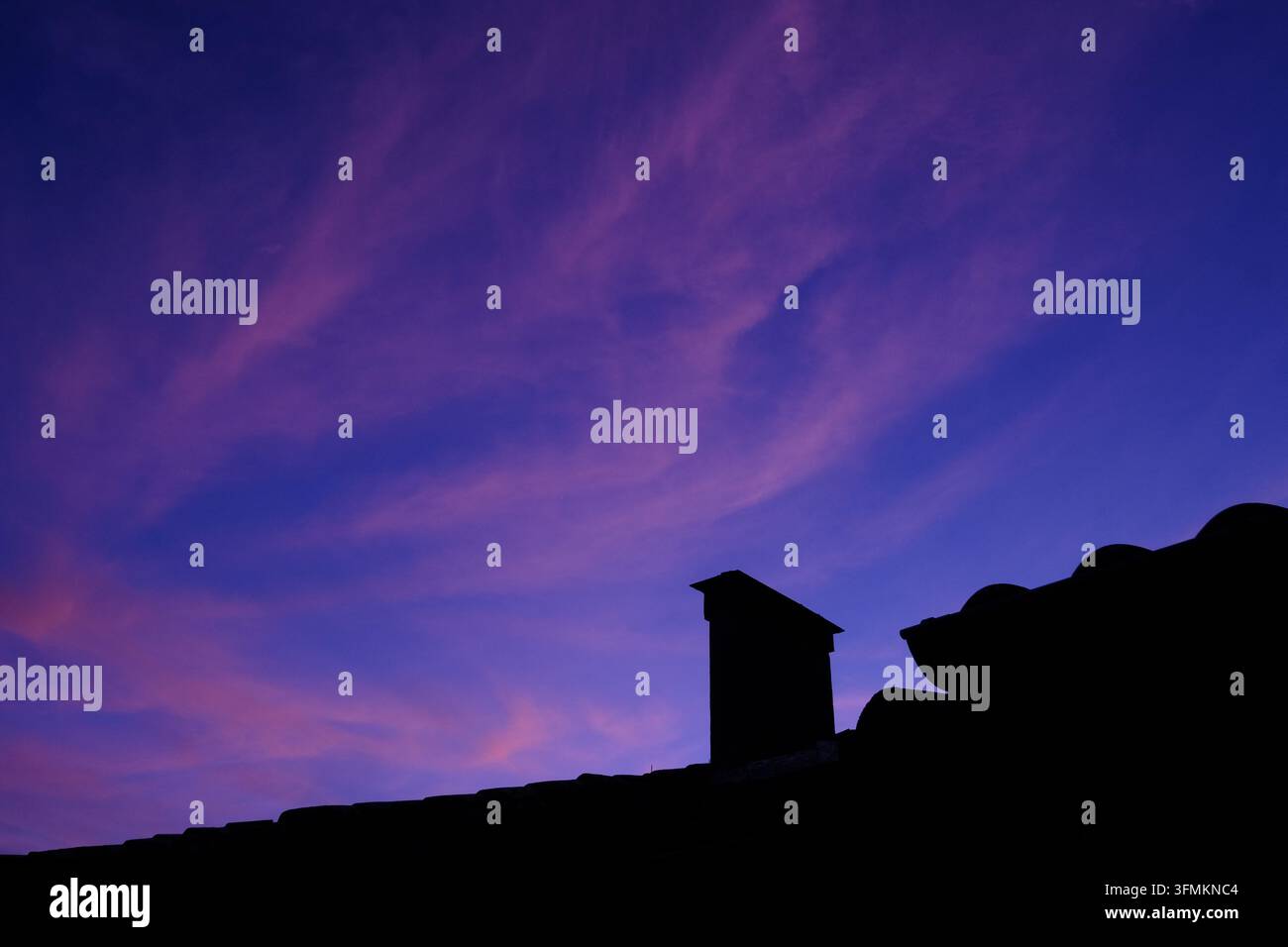A dramatic sunset illuminates the sky with scattered clouds over ...