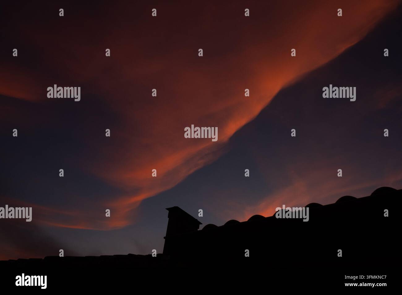 A dramatic sunset illuminates the sky with scattered clouds over ...