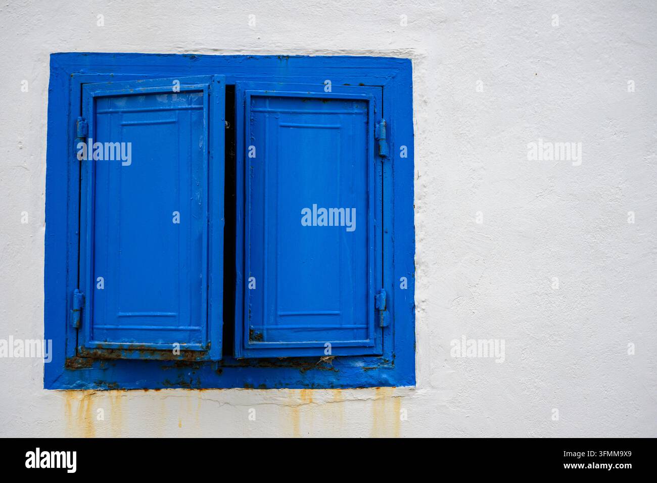 Blue window shutter slightly open on a white wall Stock Photo