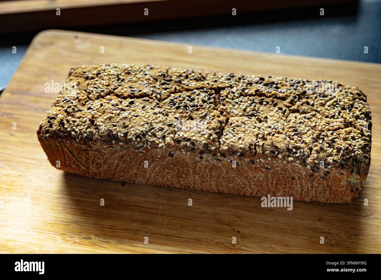 Rectangular multigrain loaf covered with mixed seeds, resting on a wooden cutting board. Stock Photo