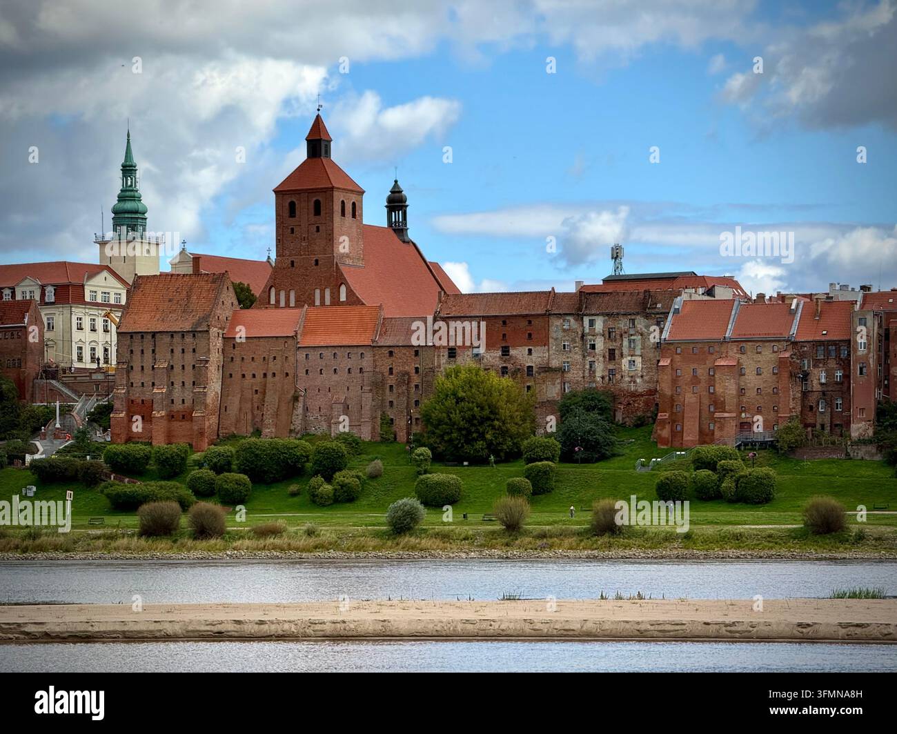 Close-up view of the historic red-brick granaries and towers of Grudziądz, Poland, rising above a grassy slope along the Vistula River under a cloudy - Smartphone Captured Stock Image