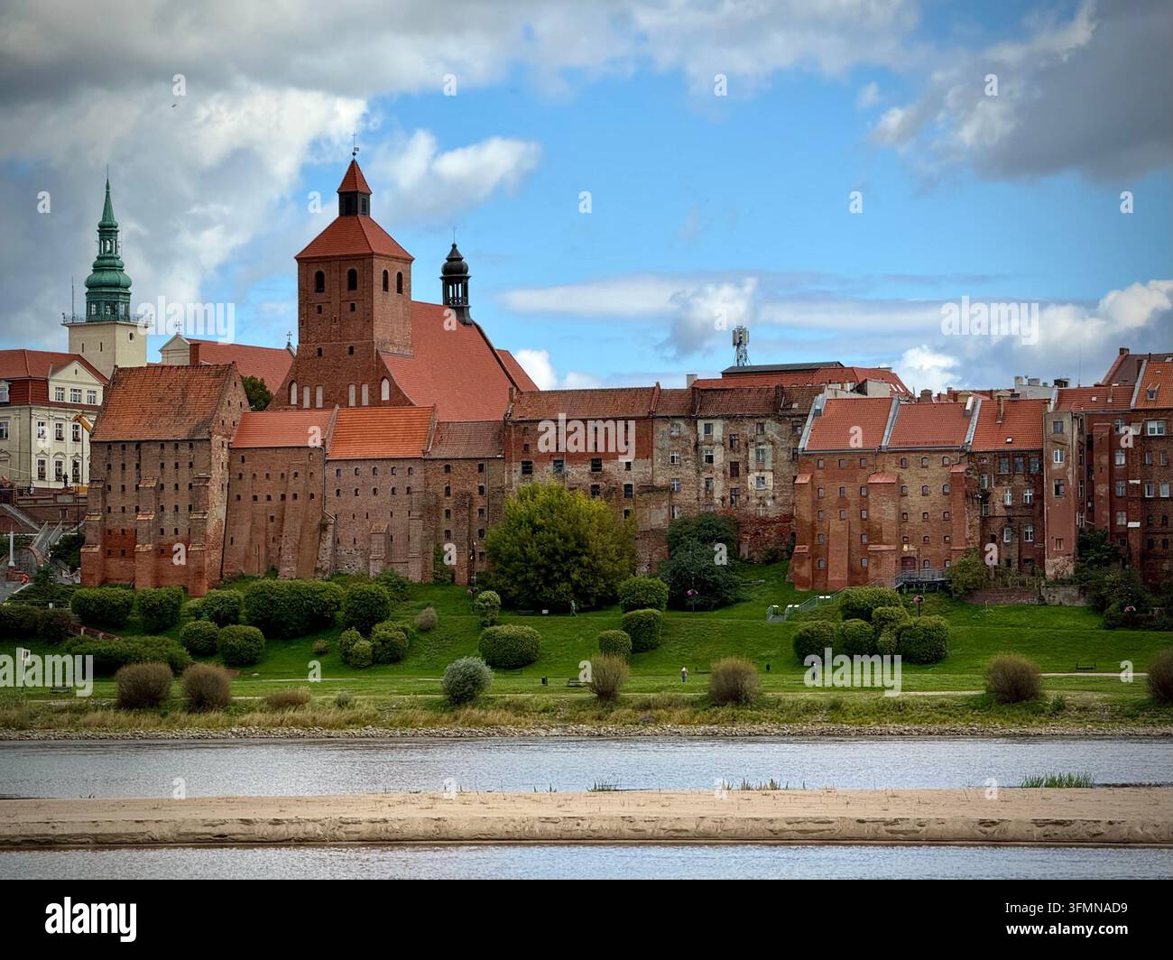 Close-up view of the historic red-brick granaries and towers of Grudziądz, Poland, rising above a grassy slope along the Vistula River under a cloudy - Smartphone Captured Stock Image
