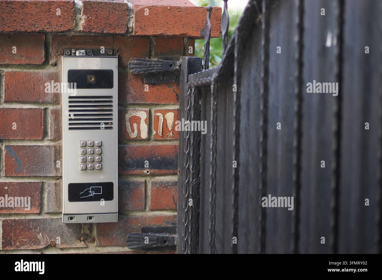 Intercom system mounted on a brick wall near a metal gate Stock Photo