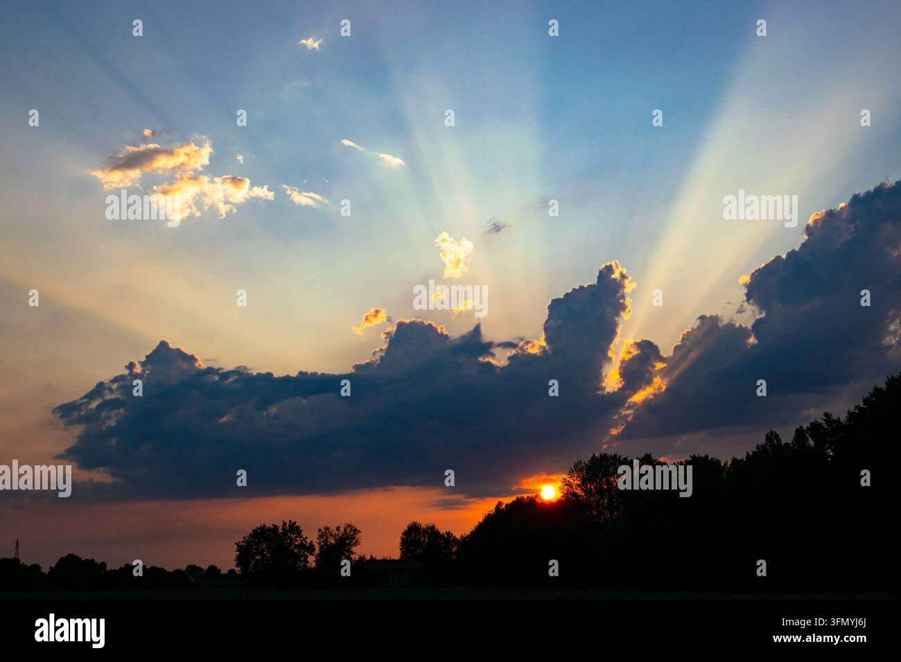 Sunrays or crepuscular rays from behind the clouds during a colorful sunset. Stock Photo