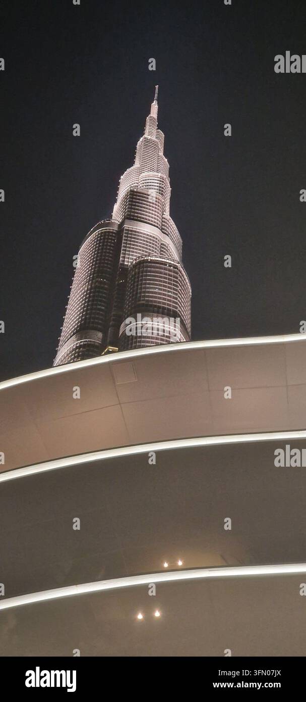 A dramatic nighttime photograph showcases the Burj Khalifa towering against a dark sky. The building is illuminated with a warm glow, creating a sense Stock Photo