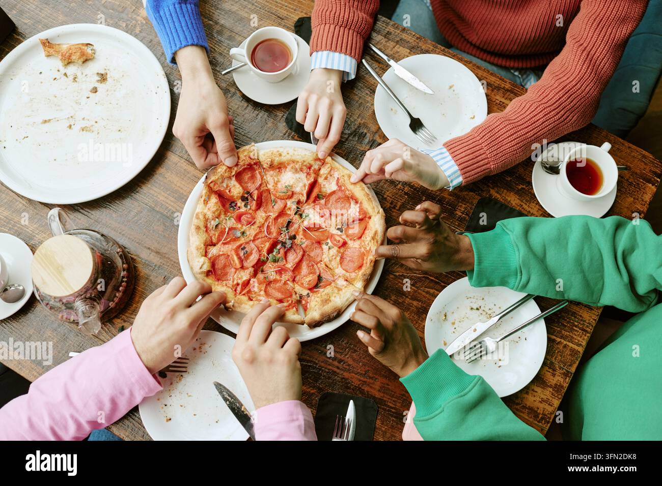 Diverse Group of Friends Sharing Pizza Slices in Cafe Stock Photo