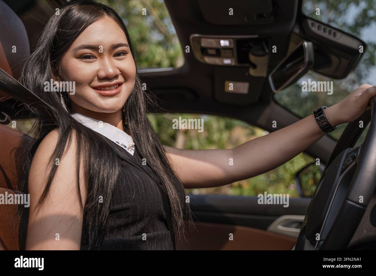 Smiling young Asian woman holding the steering wheel while driving her modern car. Stock Photo