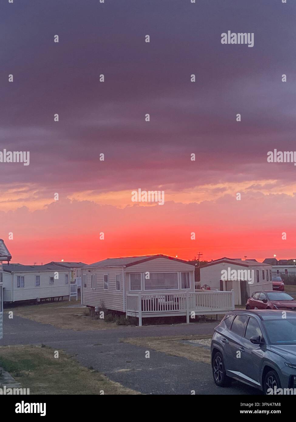 Lovely pink and purple gradient sky from the balcony of a cute caravan park in England. Beautiful evening view of the sun setting in the background - Smartphone Captured Stock Image