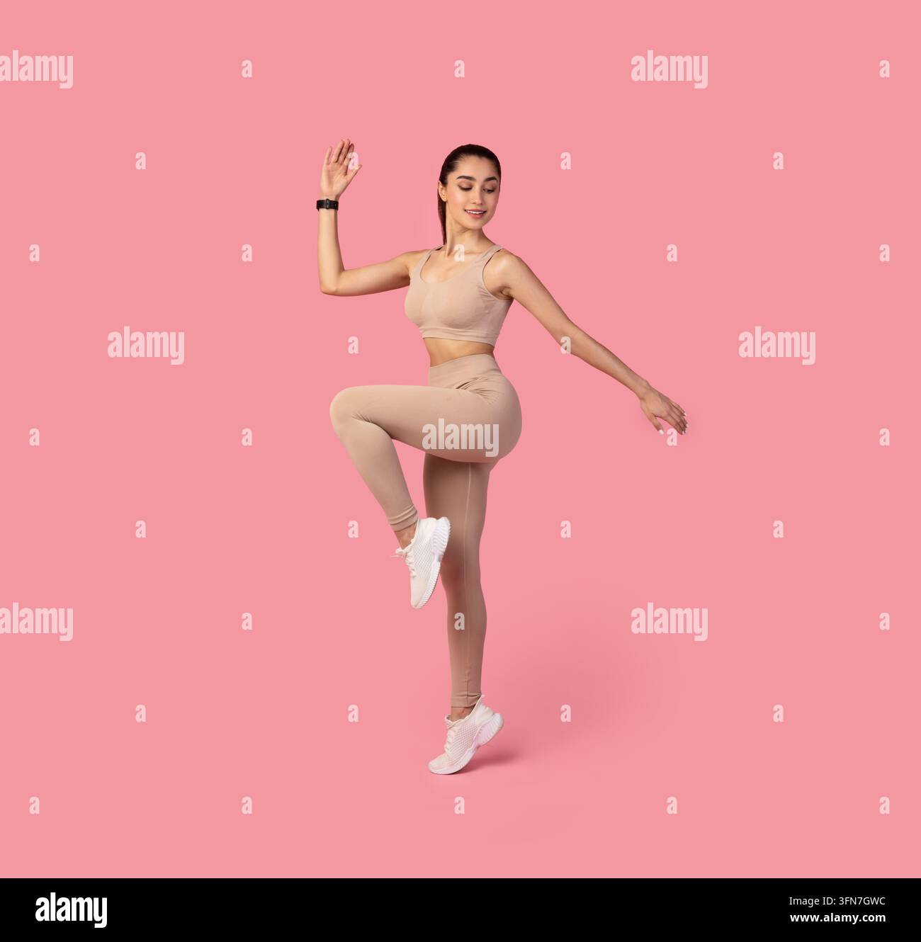 Balance And Endurance. Studio shot of beautiful young sportswoman standing on one leg, doing exercise, standing in high knee pose isolated over pink b Stock Photo