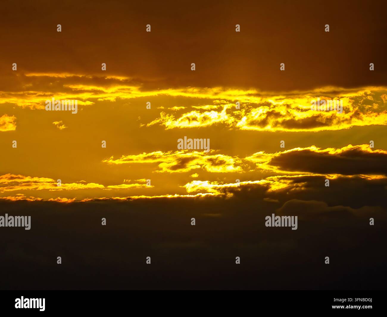 Intense golden sunset sky with dramatic dark cloud layers and glowing light streaks with copy space Stock Photo