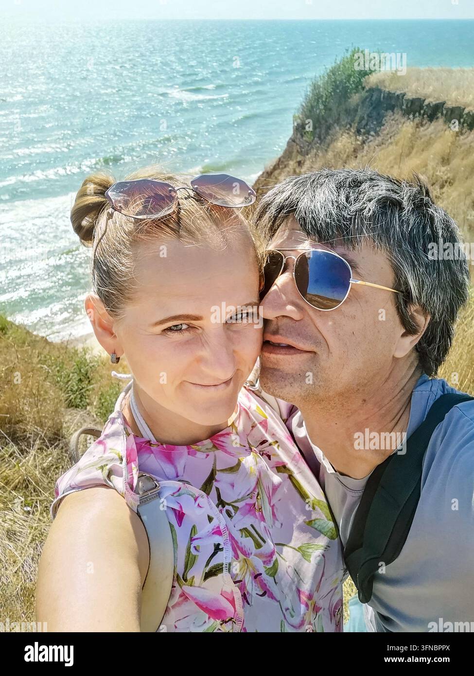 Happy romantic couple taking selfie on cliff edge over Black Sea in Odesa region, Ukraine. Summer vacation, love and lifestyle travel concept - Smartphone Captured Stock Image