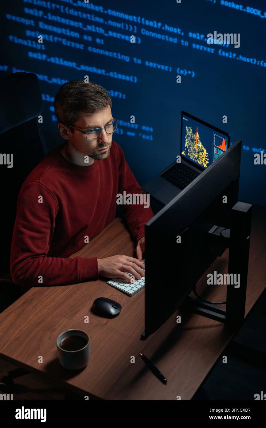 Coder or data scientist in glasses working at dark workspace with multiple monitors. Software engineer types script on keyboard, working on AI development project. Copy space.  Stock Photo