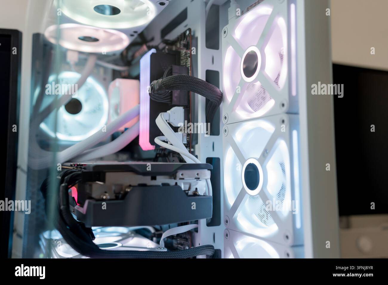 Close-up view of a white gaming computer case with illuminated RGB cooling fans, visible graphics card, cables, and liquid cooling components in a mod Stock Photo