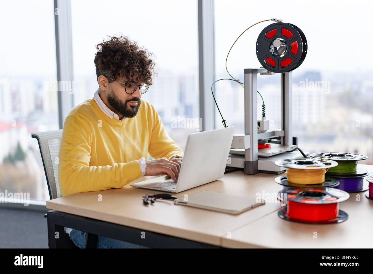 3d Man Using A Computer A man with curly hair and glasses works on a laptop next to a 3D ...