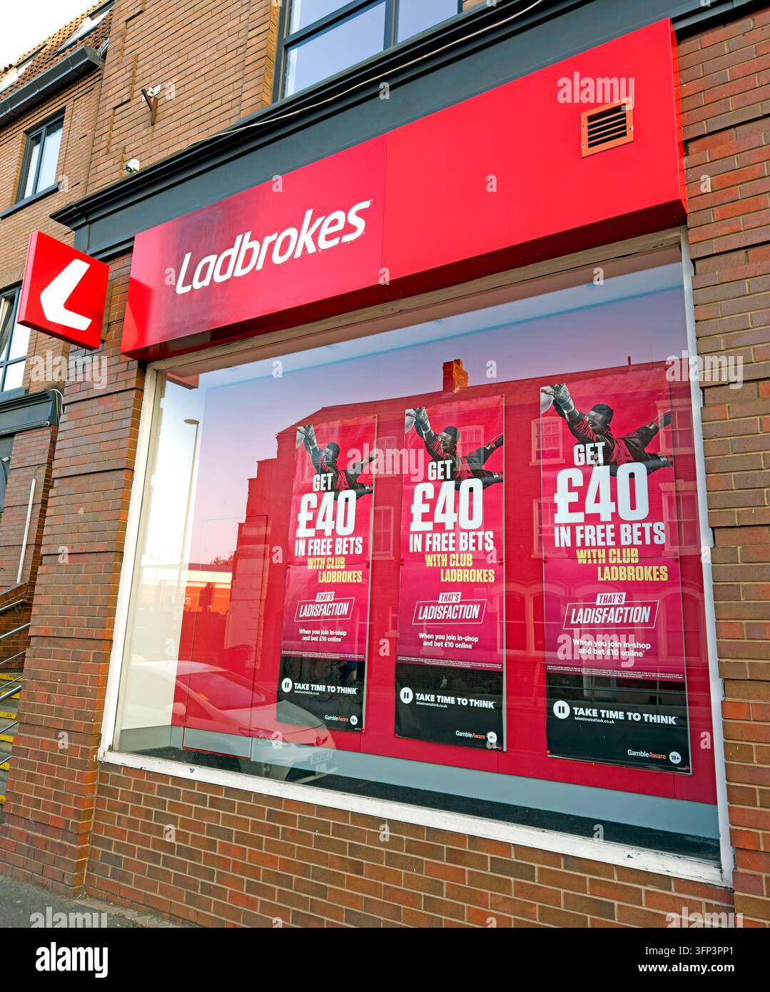 A Ladbrokes betting-shop frontage has a bright red fascia and window promotions for gambling offers. Stock Photo