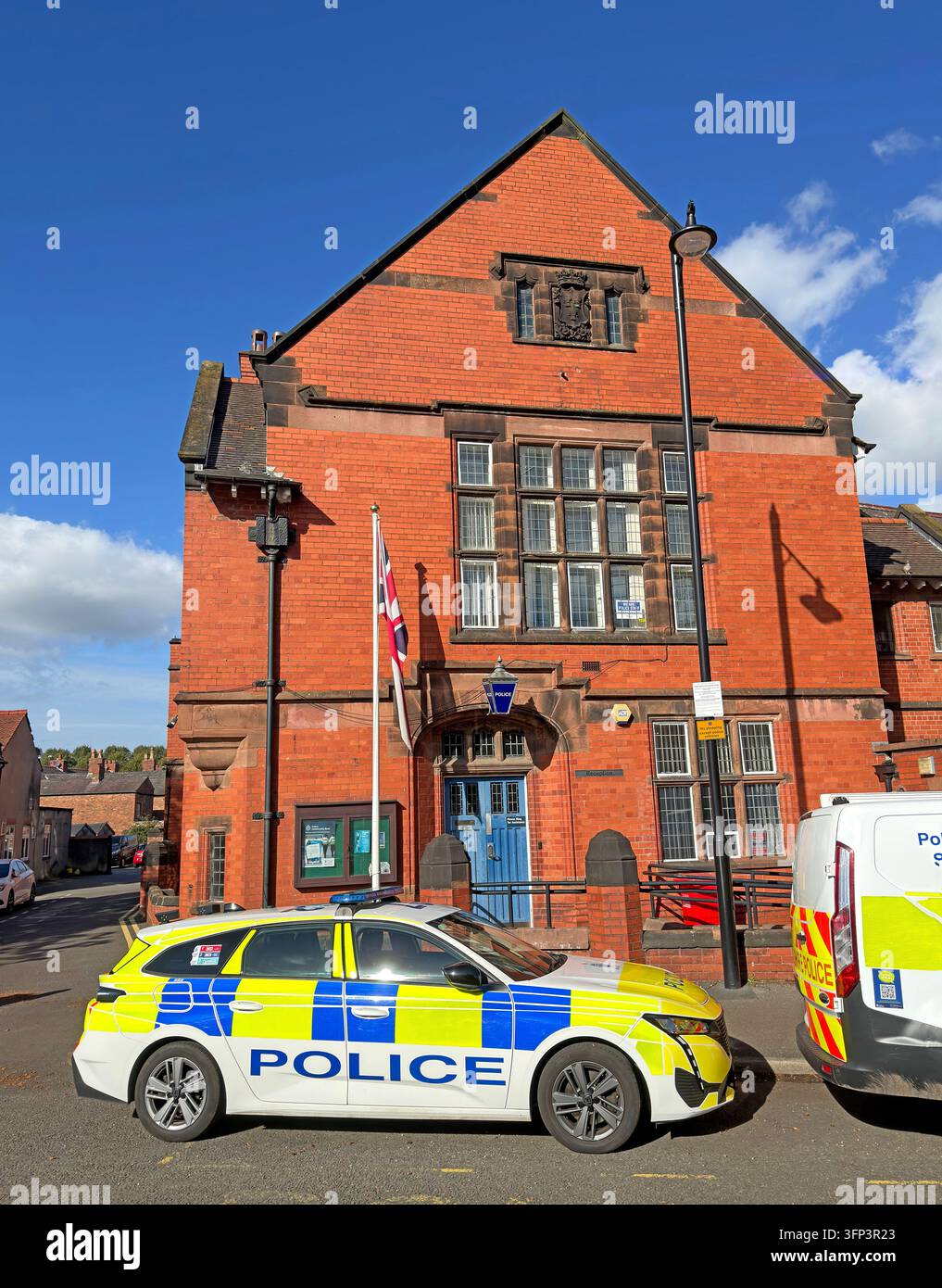 A marked Cheshire Police vehicle is parked in front of a red-brick building, with another police vehicle partly visible. Stock Photo