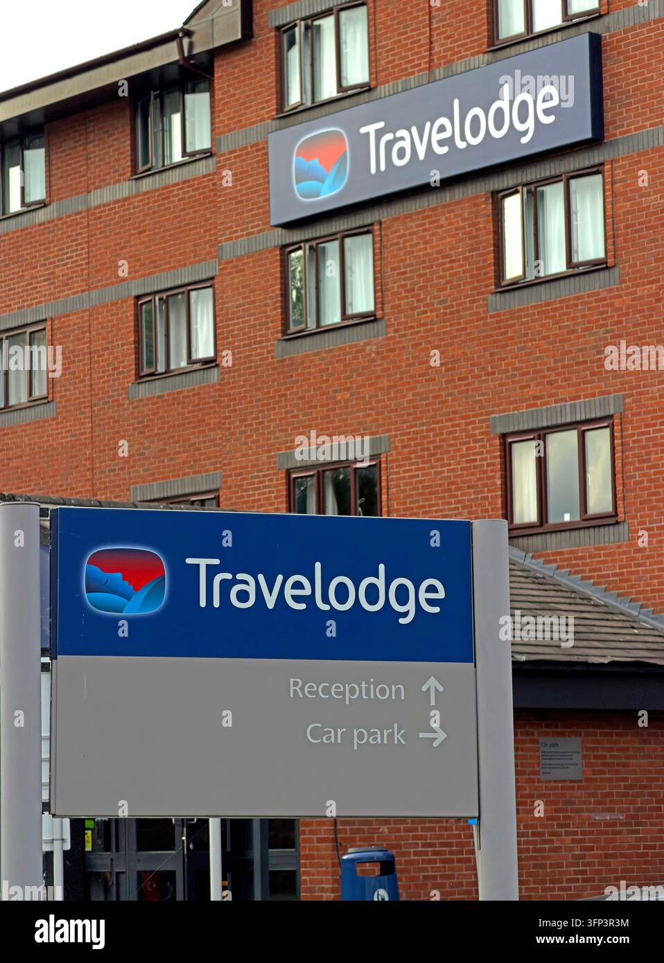 Travelodge branding appears on a central Warrington hotel building with a separate reception and car-park direction sign. Stock Photo