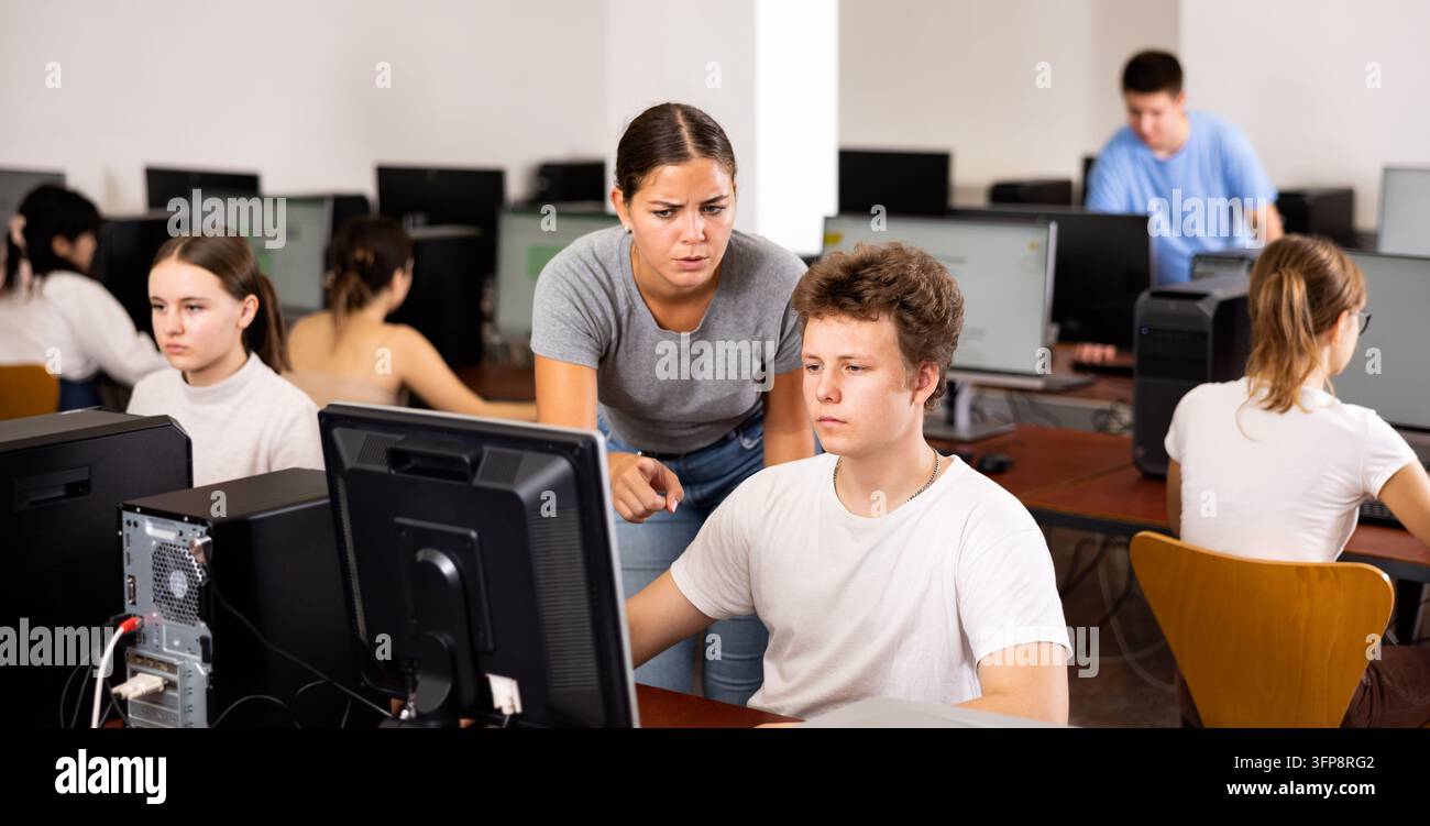 Schoolboy using computer and teacher helping to him in classroom Stock Photo